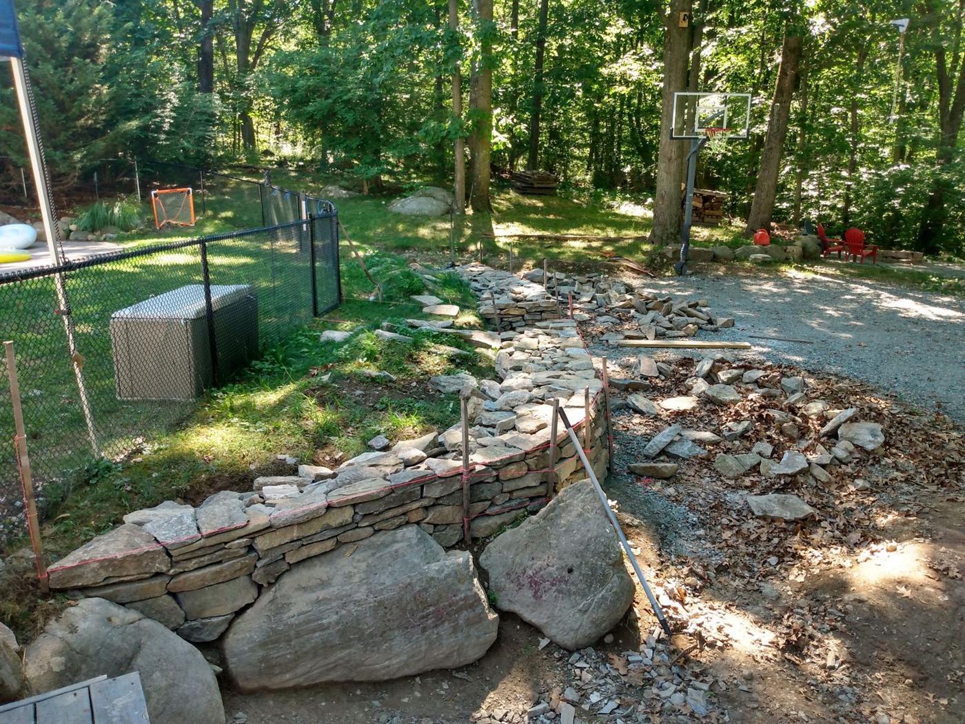 Curved dry laid stone wall going up beside a gravel drive in the woods